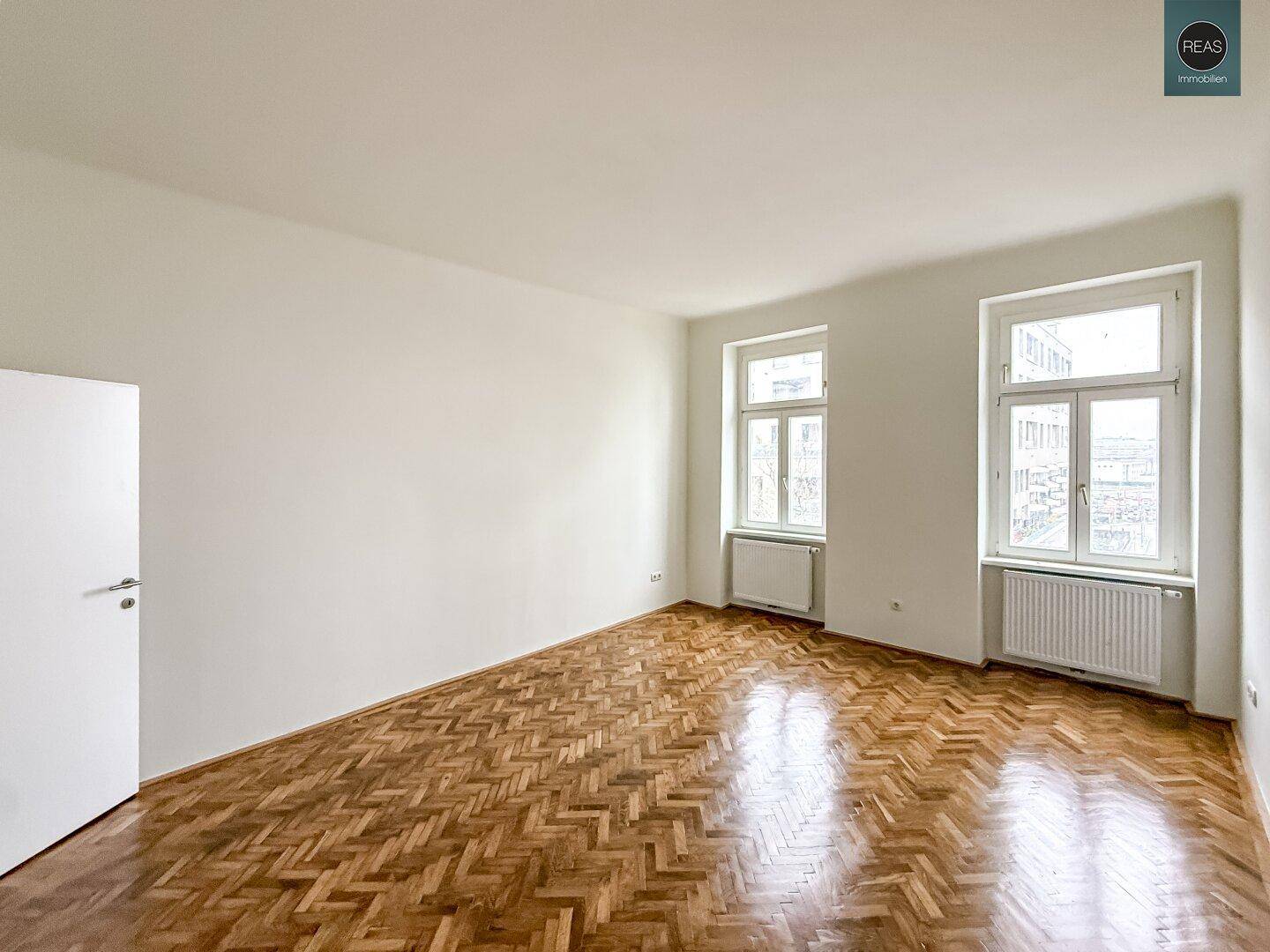Leerer Büroraum mit glänzendem Fischgrätparkett und hohen Fenstern, bereit zur individuellen Gestaltung.