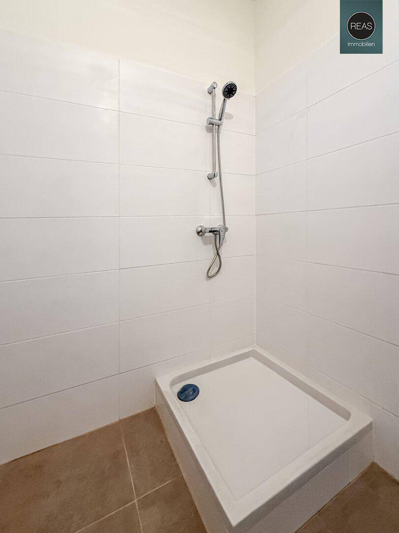 Modernes Badezimmer mit Duschwanne und Duscharmatur, komplett gefliest in Weiß und Beige.