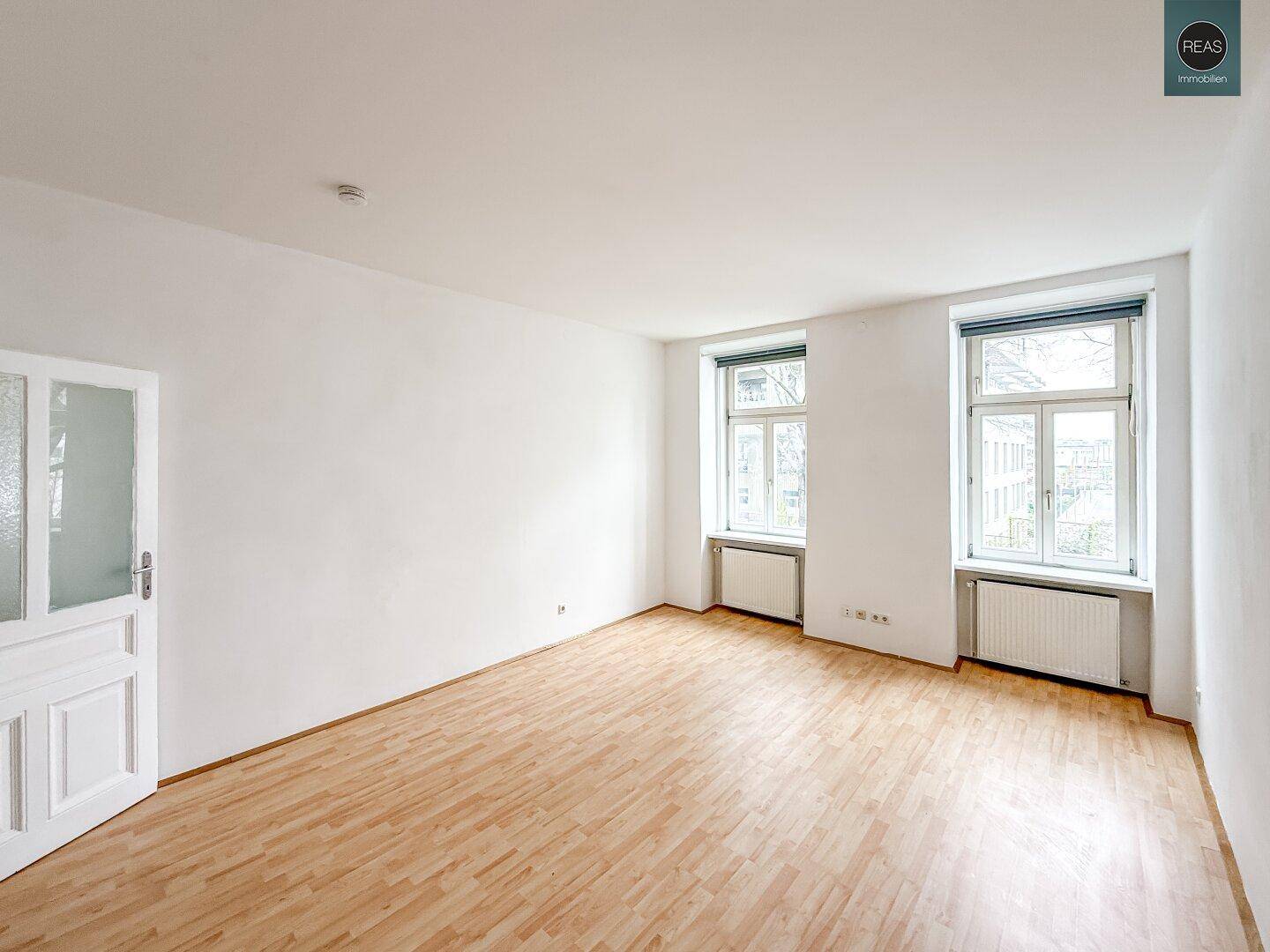 Heller, leerer Raum mit Holzboden und zwei großen Fenstern, bereit zur individuellen Gestaltung.