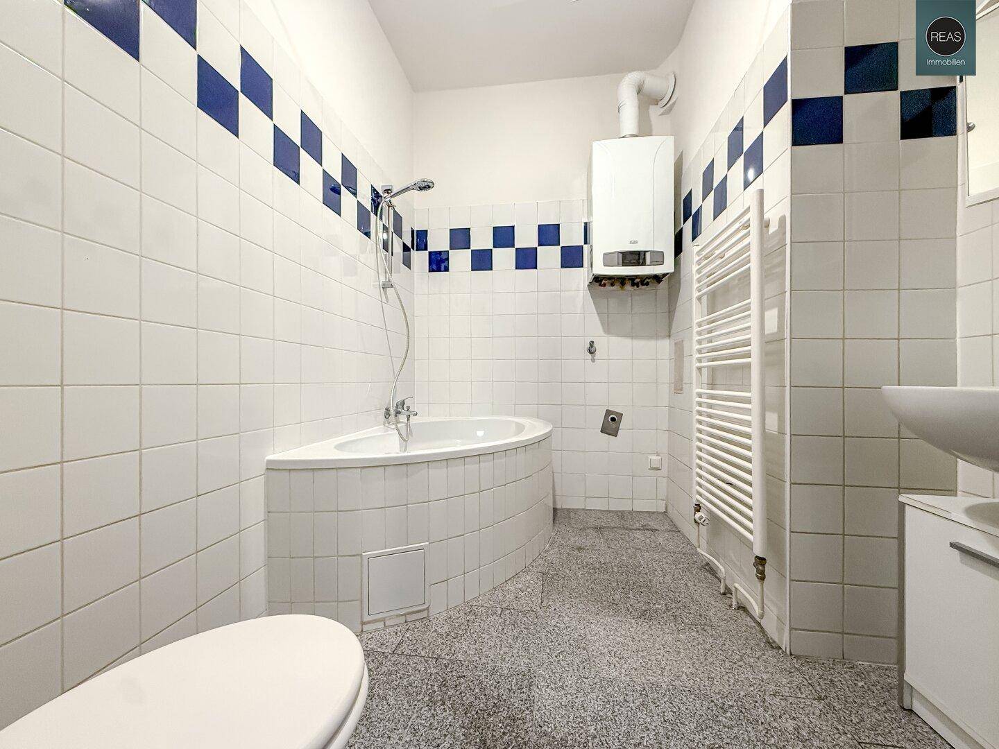 Badezimmer mit Eckbadewanne, Dusche, Handtuchheizkörper und weiß-blauen Fliesen.