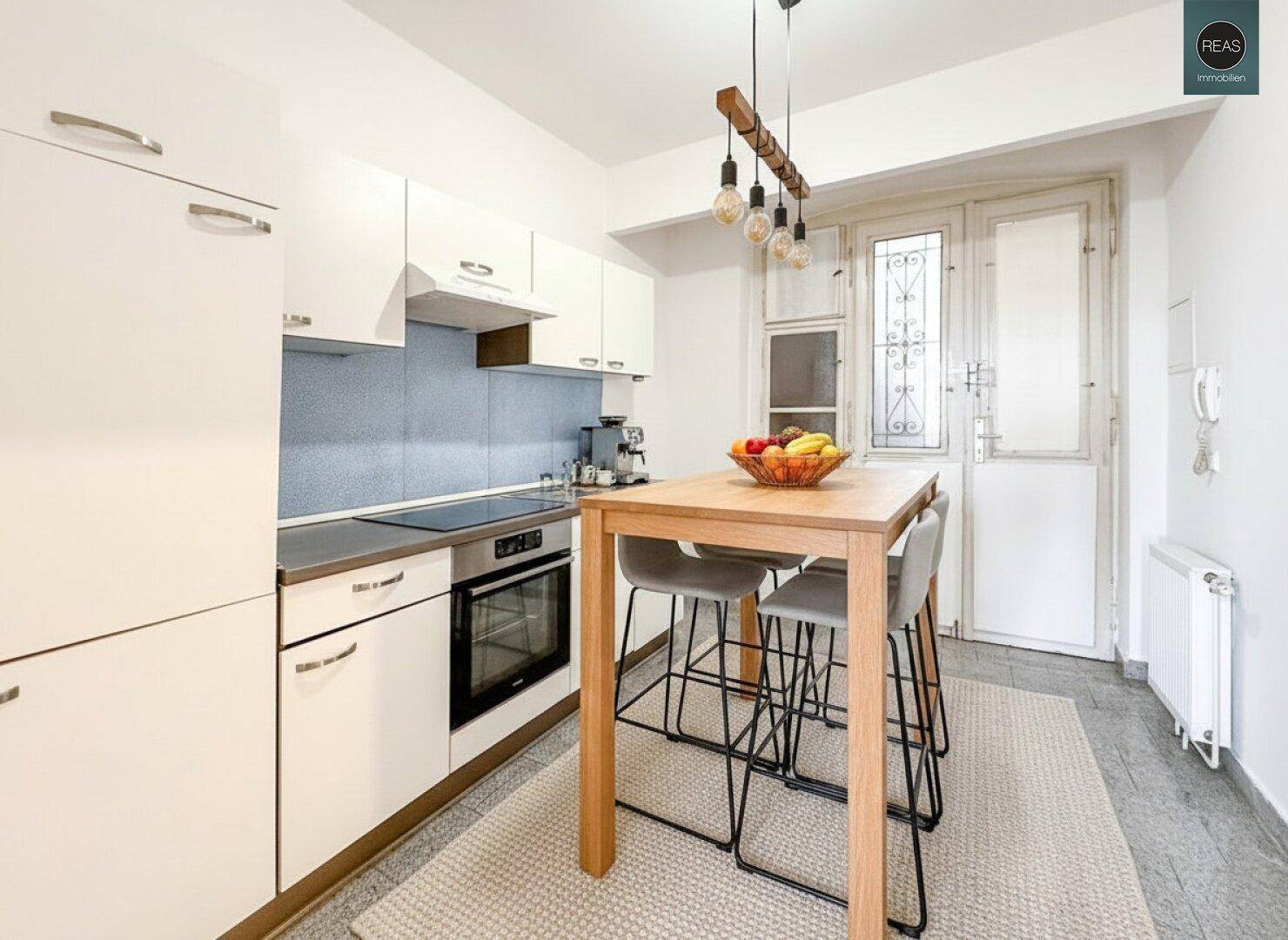 Kompakte Küche mit modernen Geräten, einem Bartisch und Zugang zu einem weiteren Bereich oder Balkon.