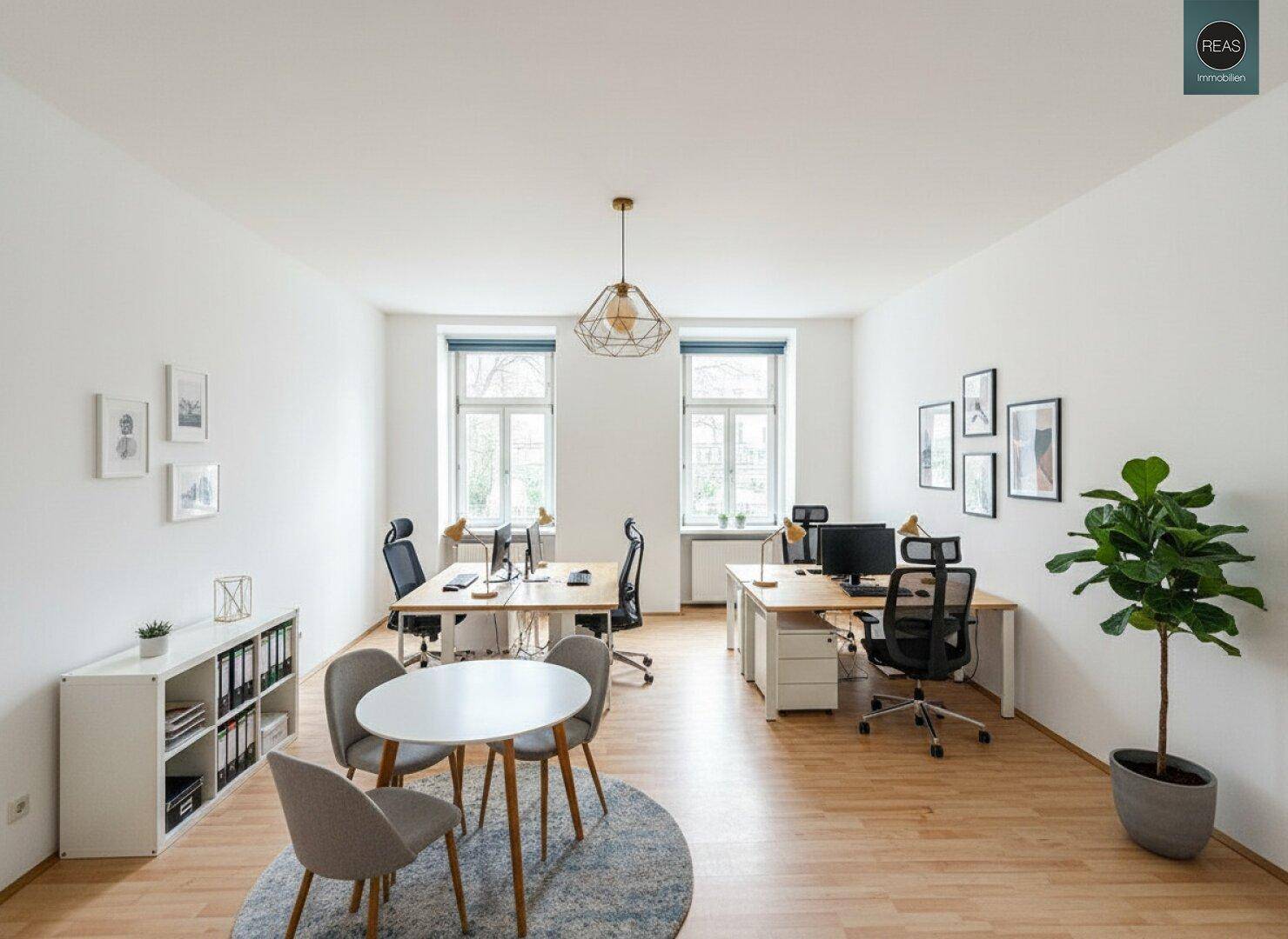 Modern eingerichtetes Büro mit zwei Arbeitsbereichen, einem kleinen Tisch und einem hellen Holzboden.