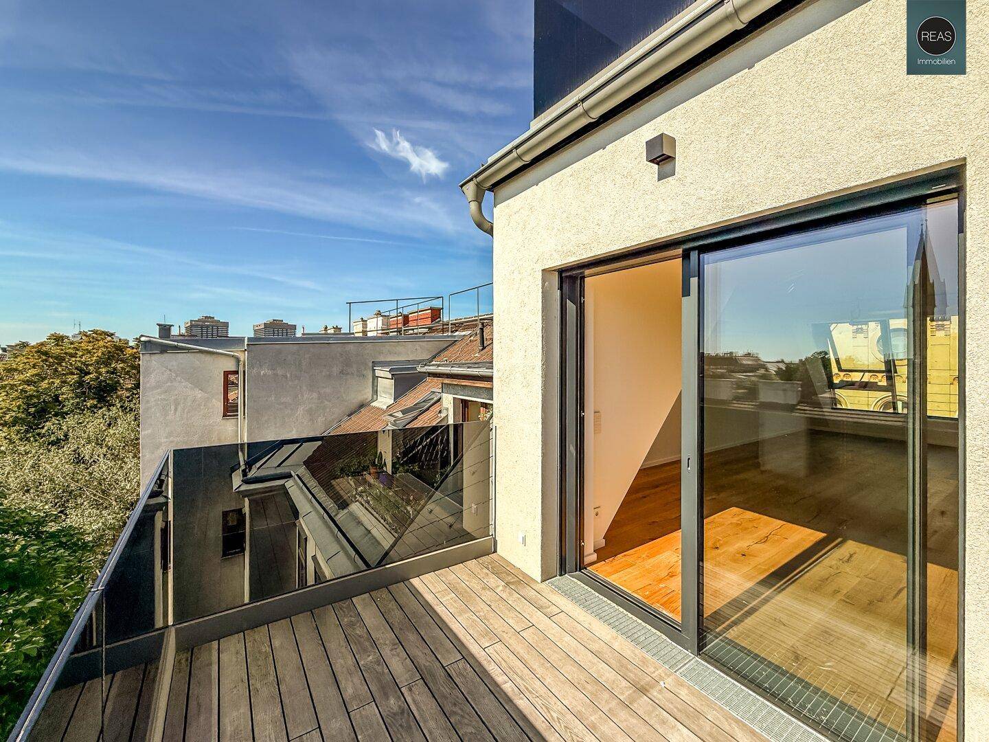 Kleiner Balkon mit Holzboden und Glasgeländer, zugänglich durch eine Glasschiebetür.