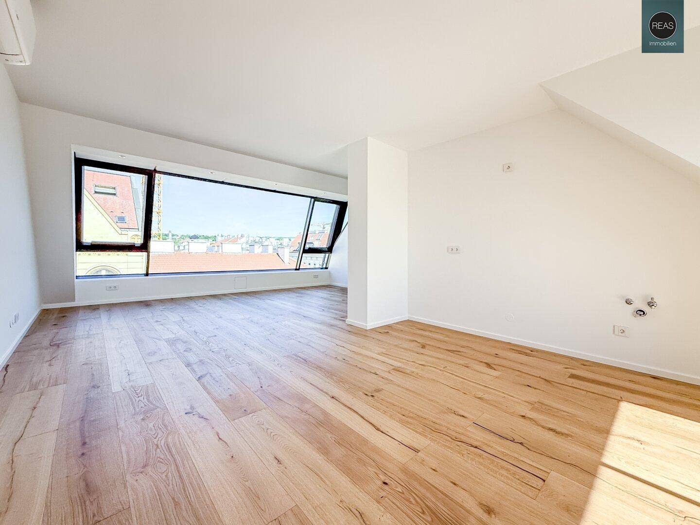 Geräumiges Zimmer mit Holzboden, Dachschrägen und breiten Fenstern mit Stadtblick.