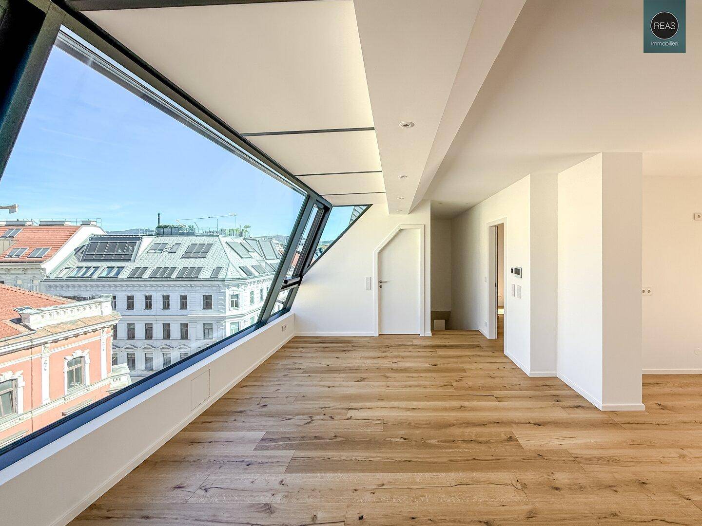 Geräumiges Zimmer mit Holzboden und schrägen Fenstern, die einen weiten Stadtblick bieten.
