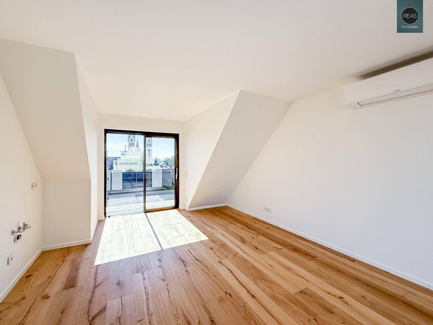 Helles Zimmer mit Holzboden, Dachschrägen und Schiebetür zum Außenbereich.