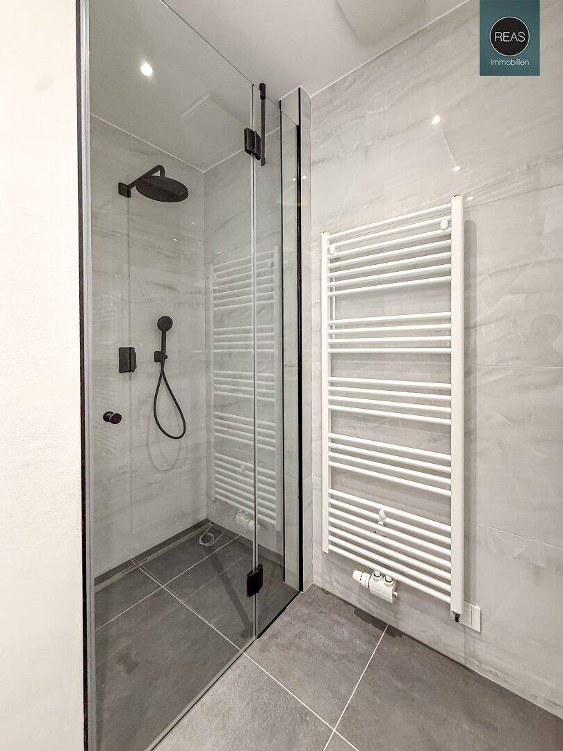Moderne begehbare Dusche mit Glasabtrennung und Regenduschkopf in einem hellen Bad.