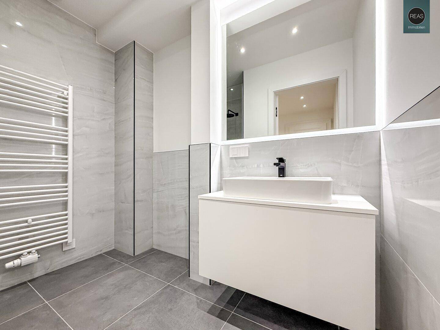 Modernes Badezimmer mit Waschtisch, beleuchtetem Spiegel und beheiztem Handtuchhalter.