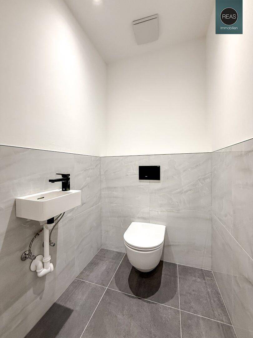 Modernes Gäste-WC mit wandhängender Toilette und kleinem Waschbecken.