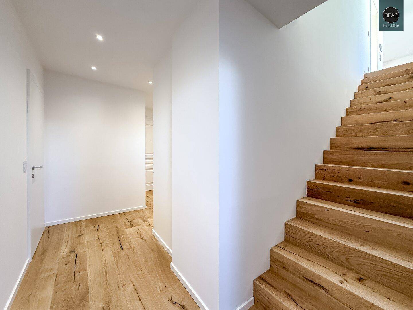 Heller Flur mit Holzboden und moderner Holztreppe, die in die obere Etage führt.