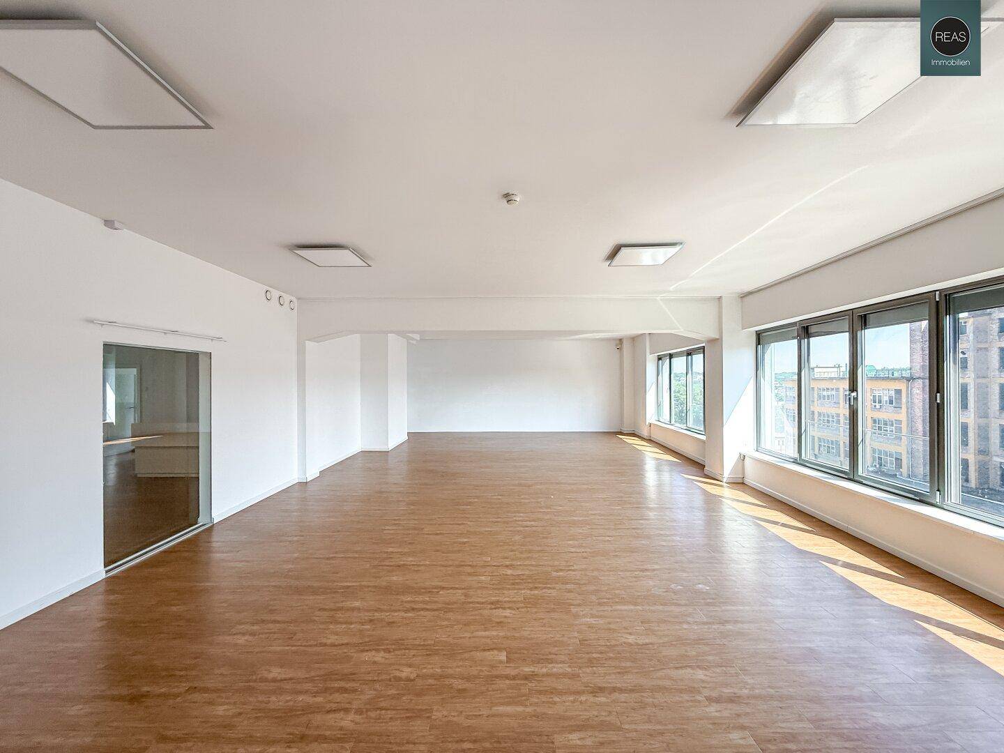 Heller, leerer Büroraum mit großen Fenstern und modernem Laminatboden, bereit zur individuellen Gestaltung.