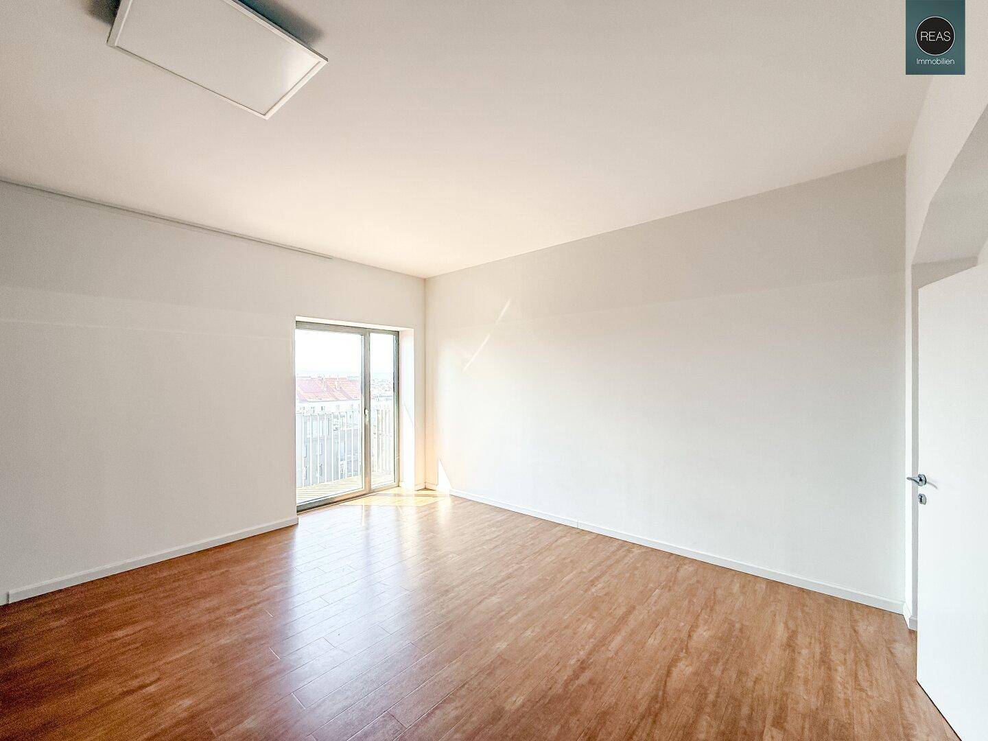 Heller Raum mit einer Glasschiebetür, die zu einem Außenbereich führt, und einem gepflegten Laminatboden.