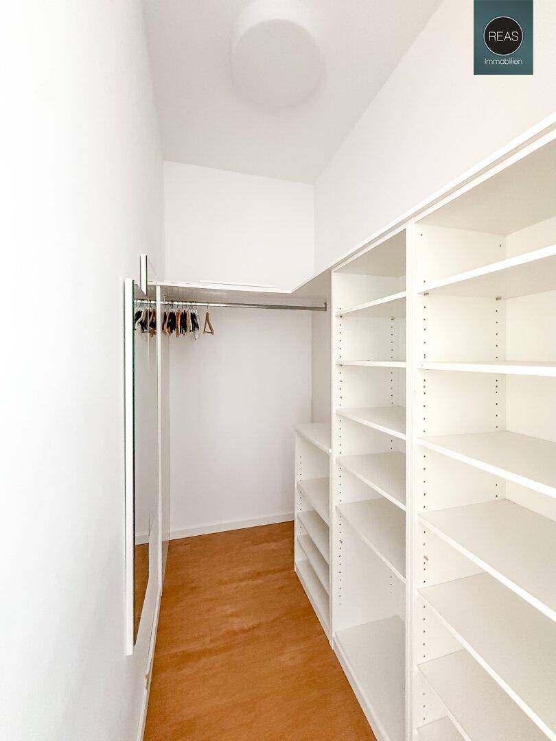 Praktischer Abstellraum oder begehbarer Kleiderschrank mit weißen Regalen und Kleiderstange.