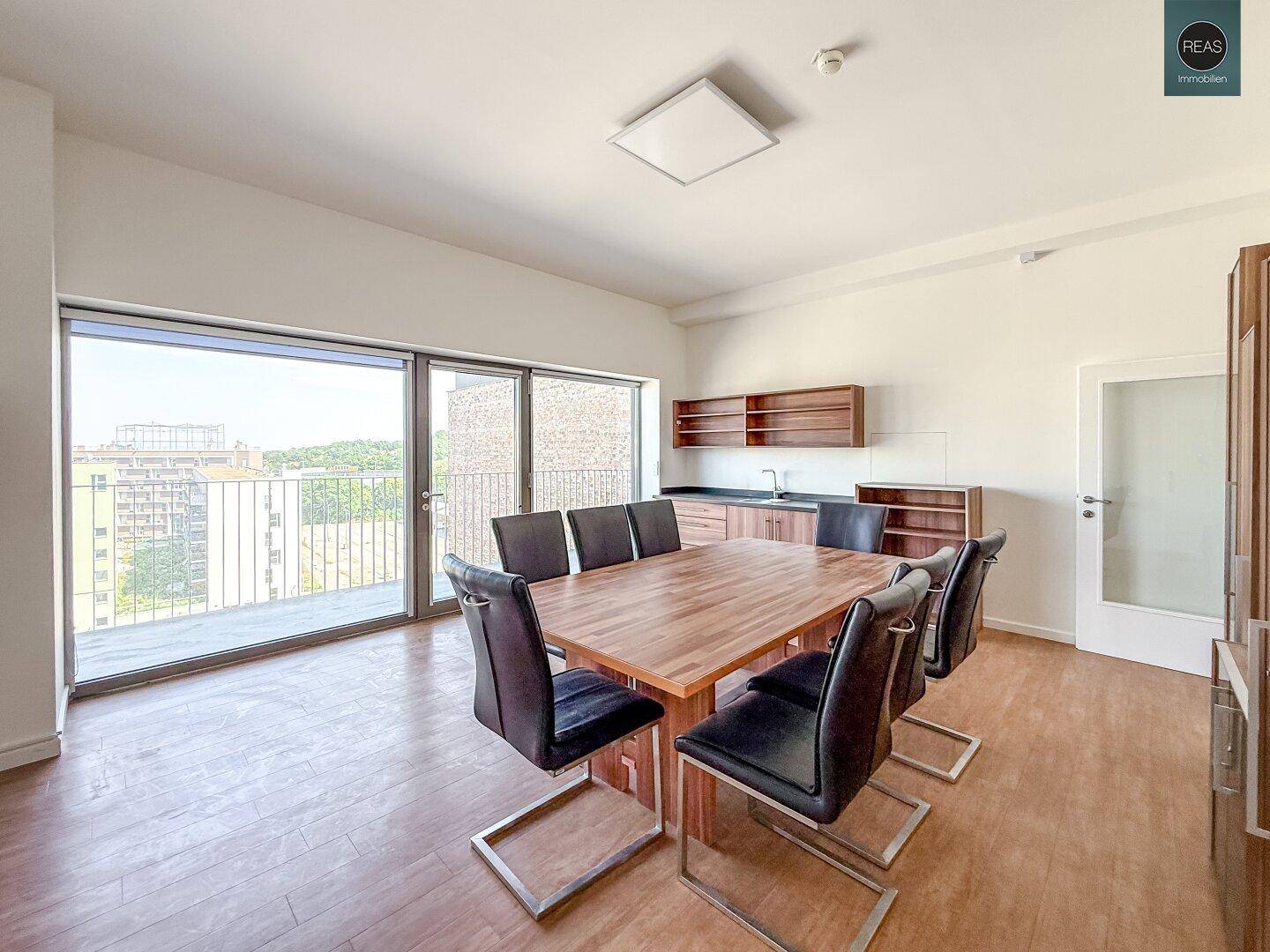 Geräumiger Essbereich mit großem Holztisch, Stühlen und einer kleinen Küchenzeile, mit Zugang zum Balkon.