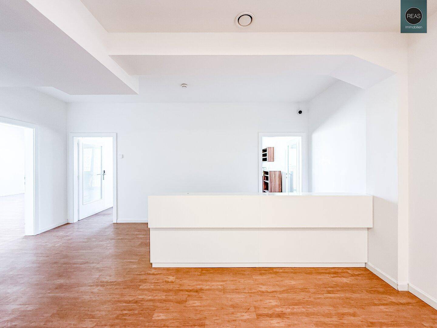 Moderner Empfangsbereich mit weißer Theke, Überwachungskamera an der Decke und hellem Laminatboden.