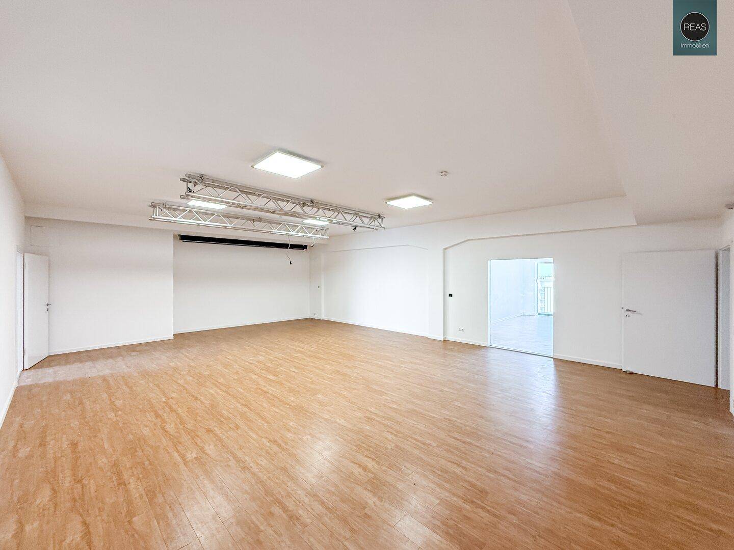 Großer, leerer Raum mit Holzboden, weißen Wänden und einer Deckenkonstruktion für Beleuchtung.