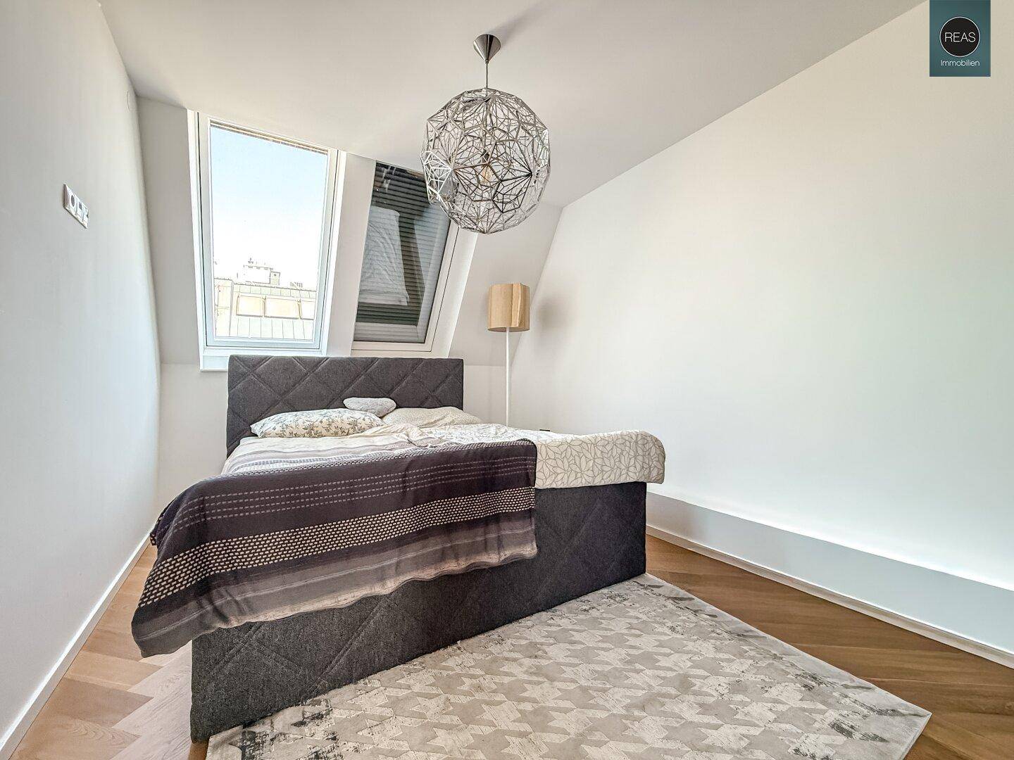 Schlafzimmer mit Doppelbett, Holzboden und Dachfenstern, die viel natürliches Licht hereinlassen.