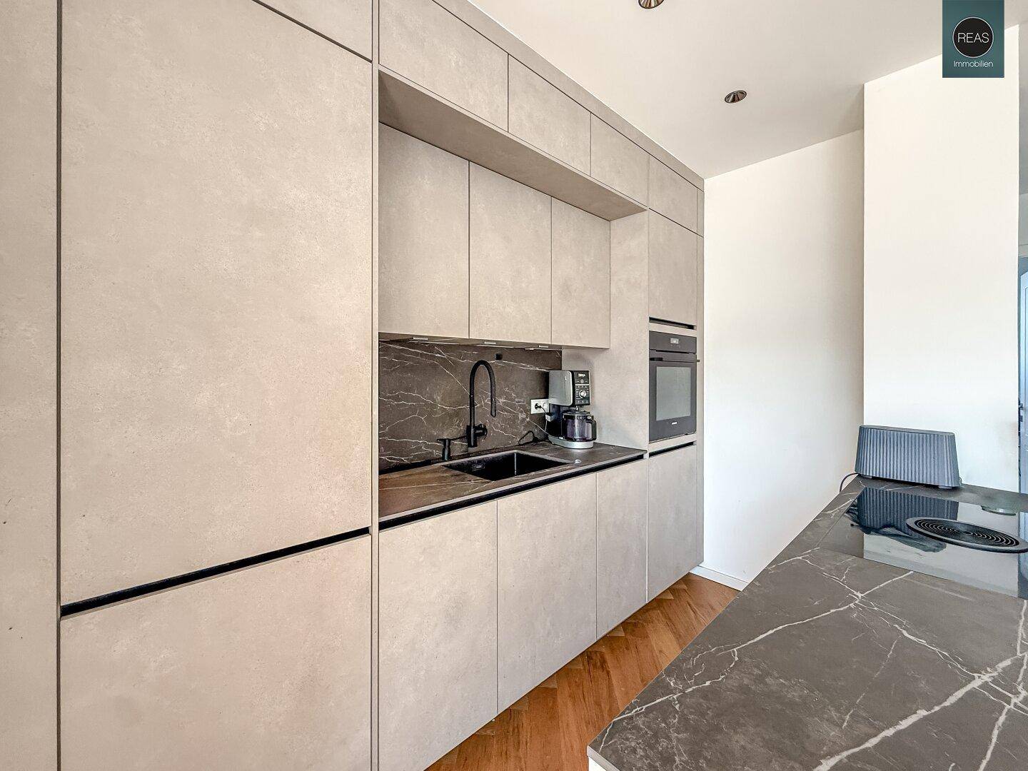 Detailansicht der modernen Küche mit Spüle, Kochfeld und integrierten Geräten in schlichtem Design.