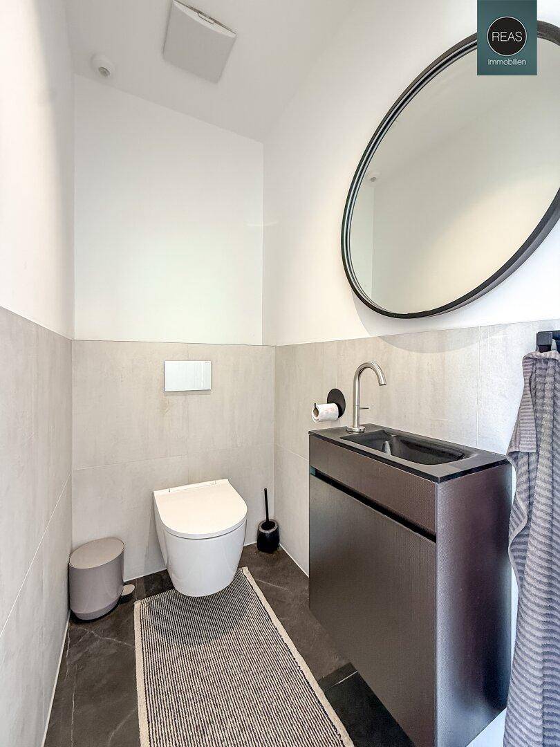 Modernes Gäste-WC mit Wand-WC, kleinem Waschbecken und dunklen Fliesen.