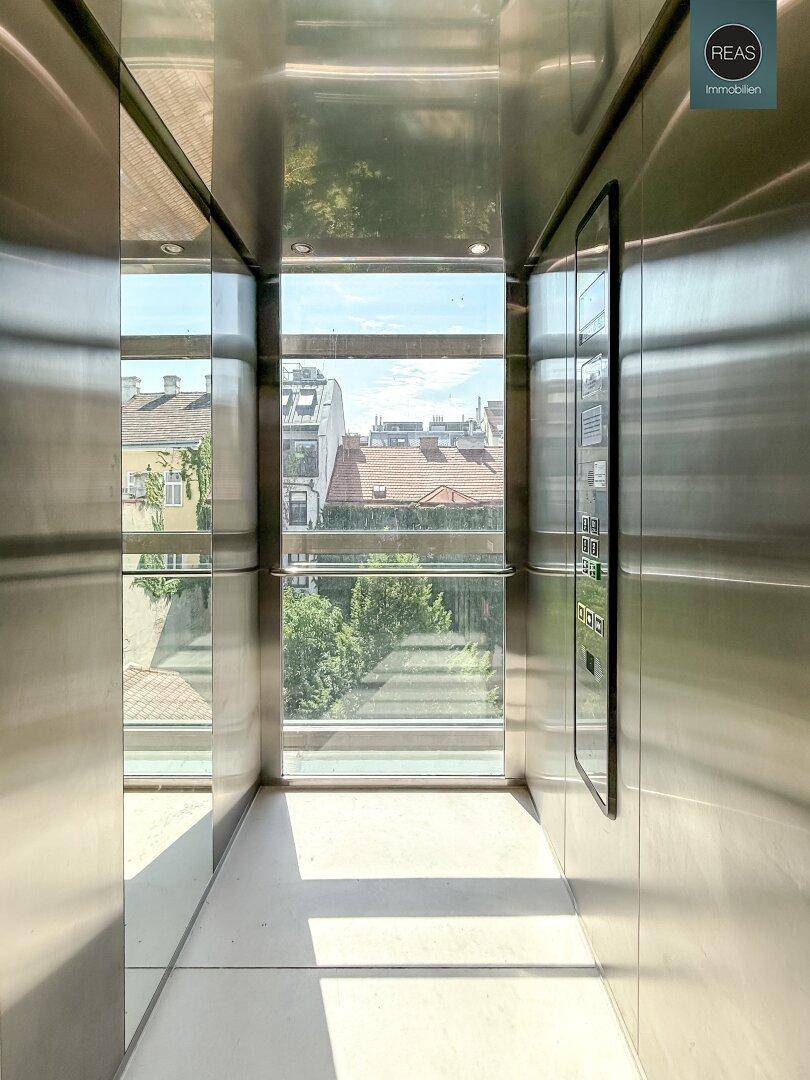 Moderner Glasaufzug mit Blick auf die umliegenden Gebäude und viel Tageslicht.