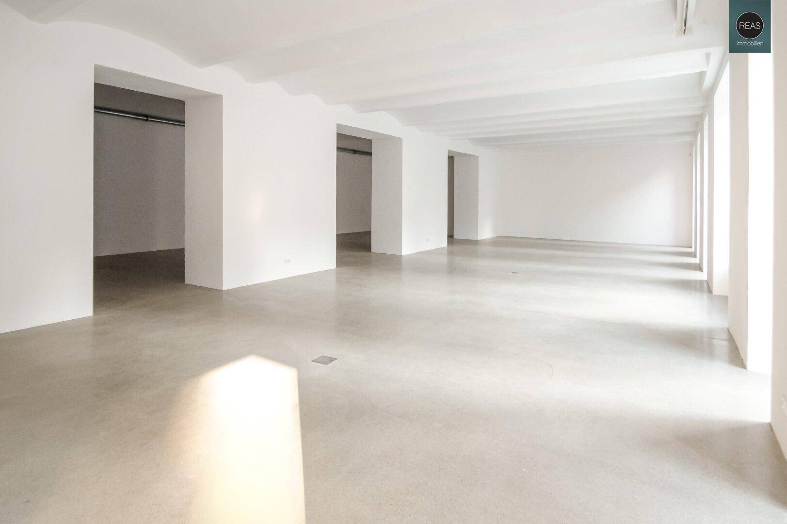 Heller, weitläufiger Büroraum mit hohen Decken, großen Fenstern und glattem Betonboden.
