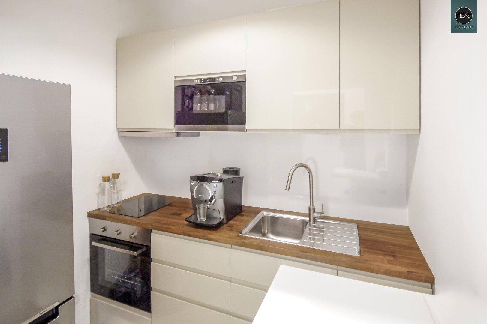 Kompakte, moderne Küchenzeile mit Holz-Arbeitsplatte, Spüle und integrierten Geräten.