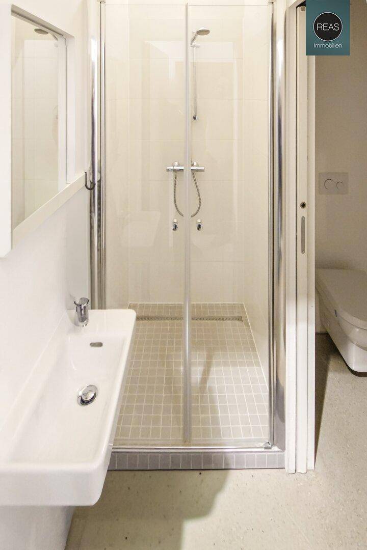 Modernes Badezimmer mit Duschkabine, Waschbecken und hellen Fliesen.