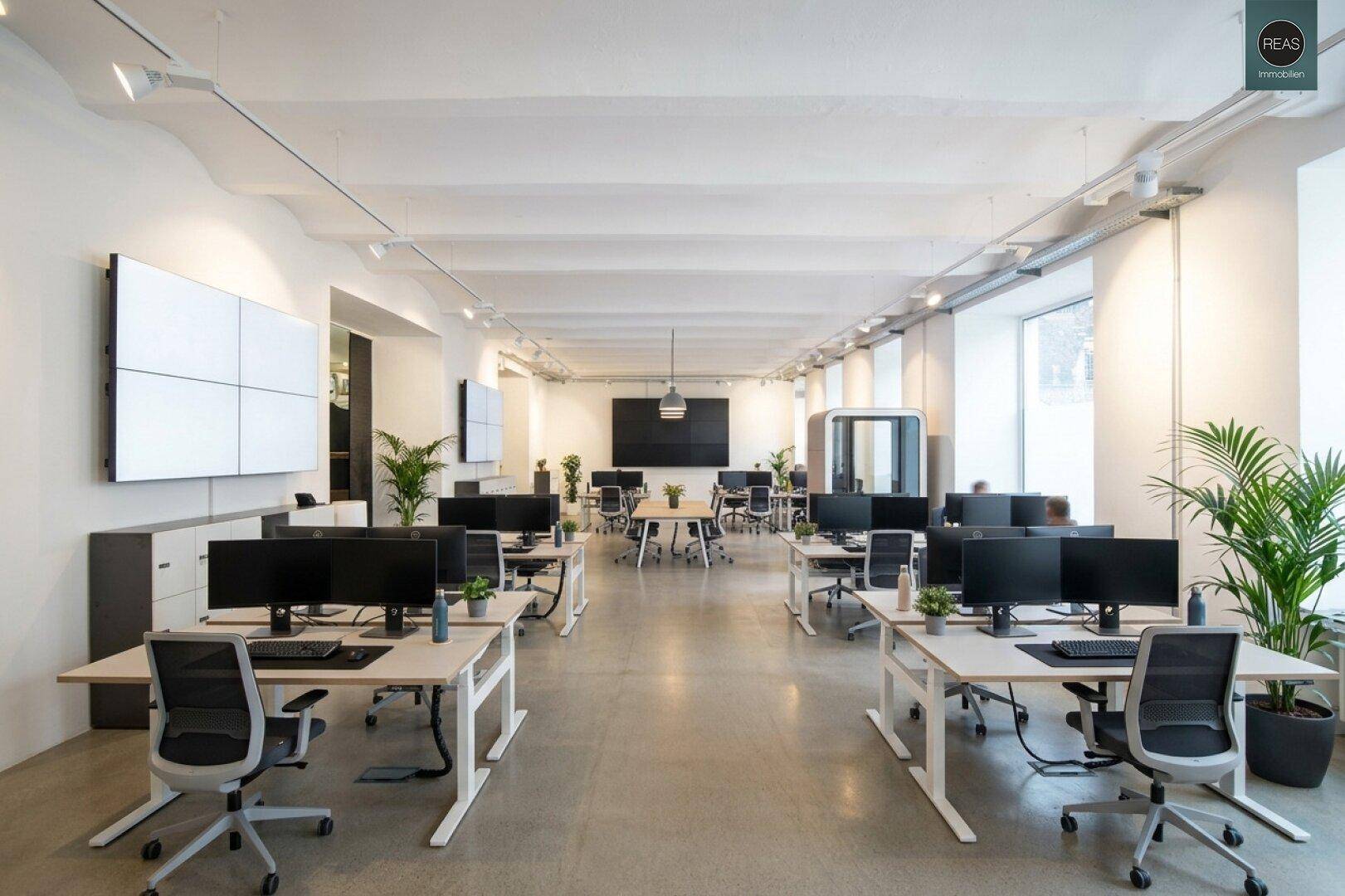 Moderner Großraumbüro mit ergonomischen Arbeitsplätzen, Pflanzen und großen Bildschirmen.