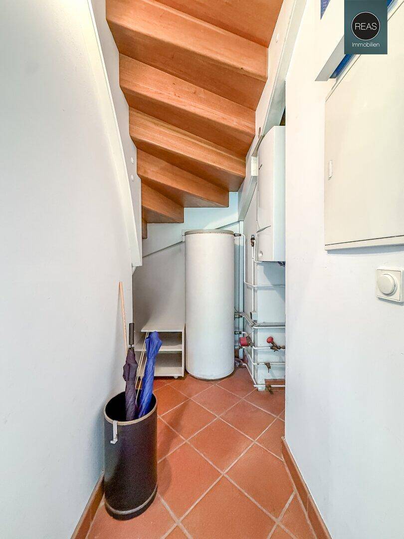 Abstellraum unter der Treppe mit Warmwasserspeicher und Heizungsinstallationen auf Terrakottafliesen.