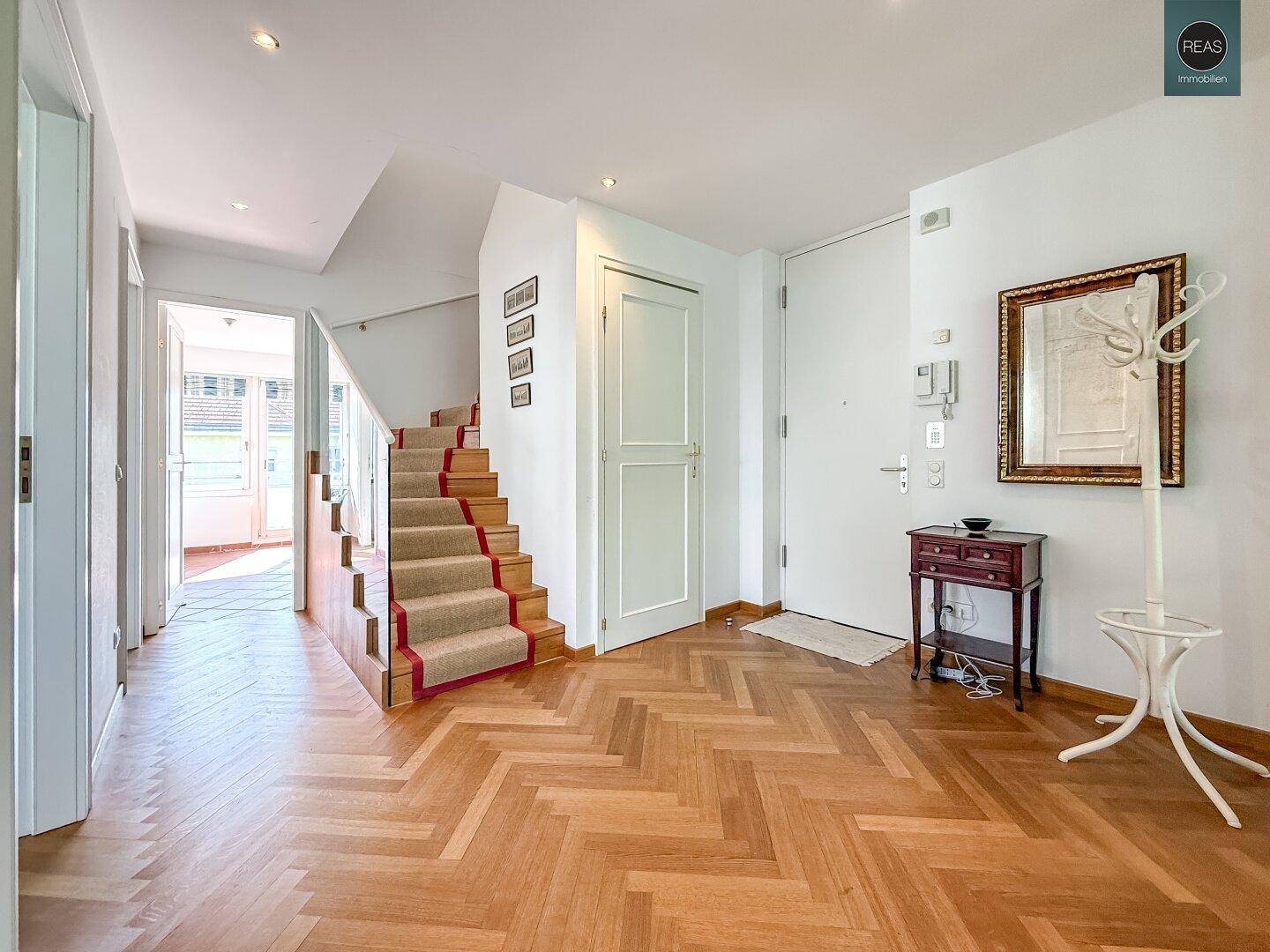 Heller Eingangsbereich mit Fischgrätparkett, Treppe und Garderobe.