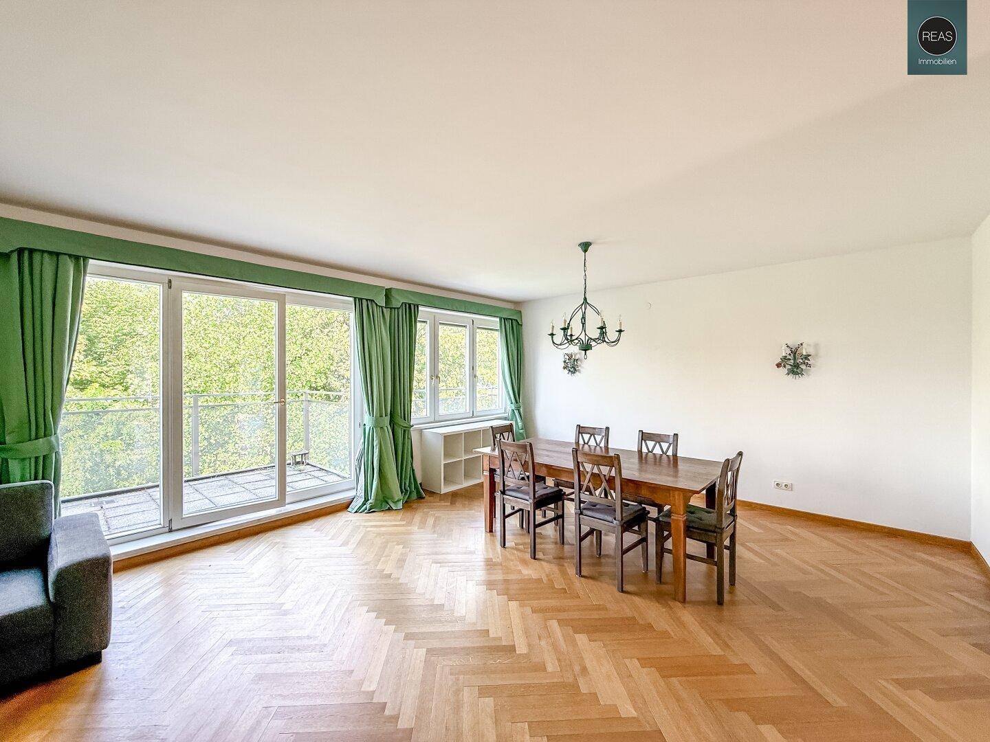 Offener Wohn- und Essbereich mit Holztisch, Parkettboden und Blick ins Grüne.