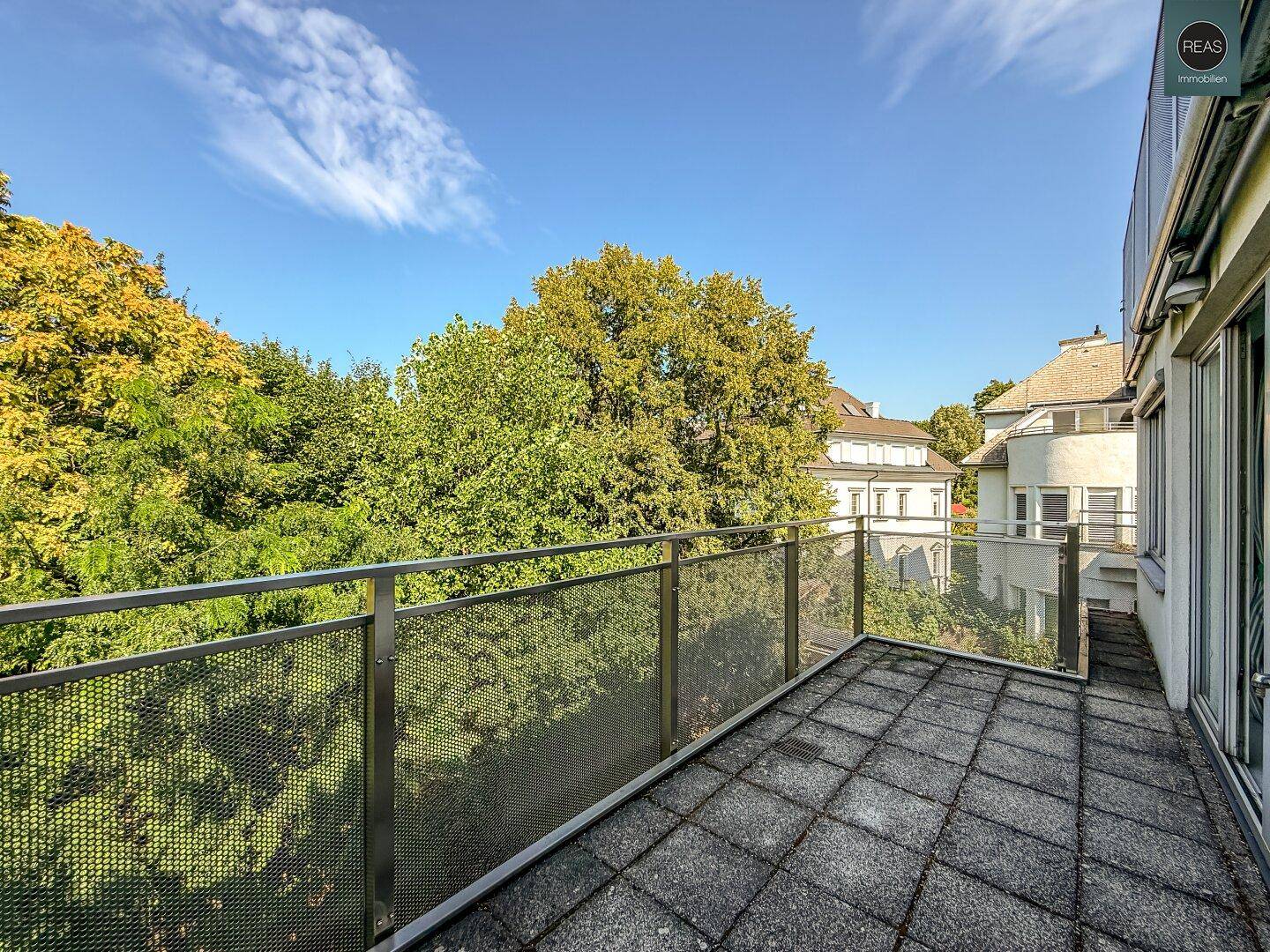 Schmaler Balkon mit Metallgeländer und Blick auf die umliegenden Bäume und Gebäude.
