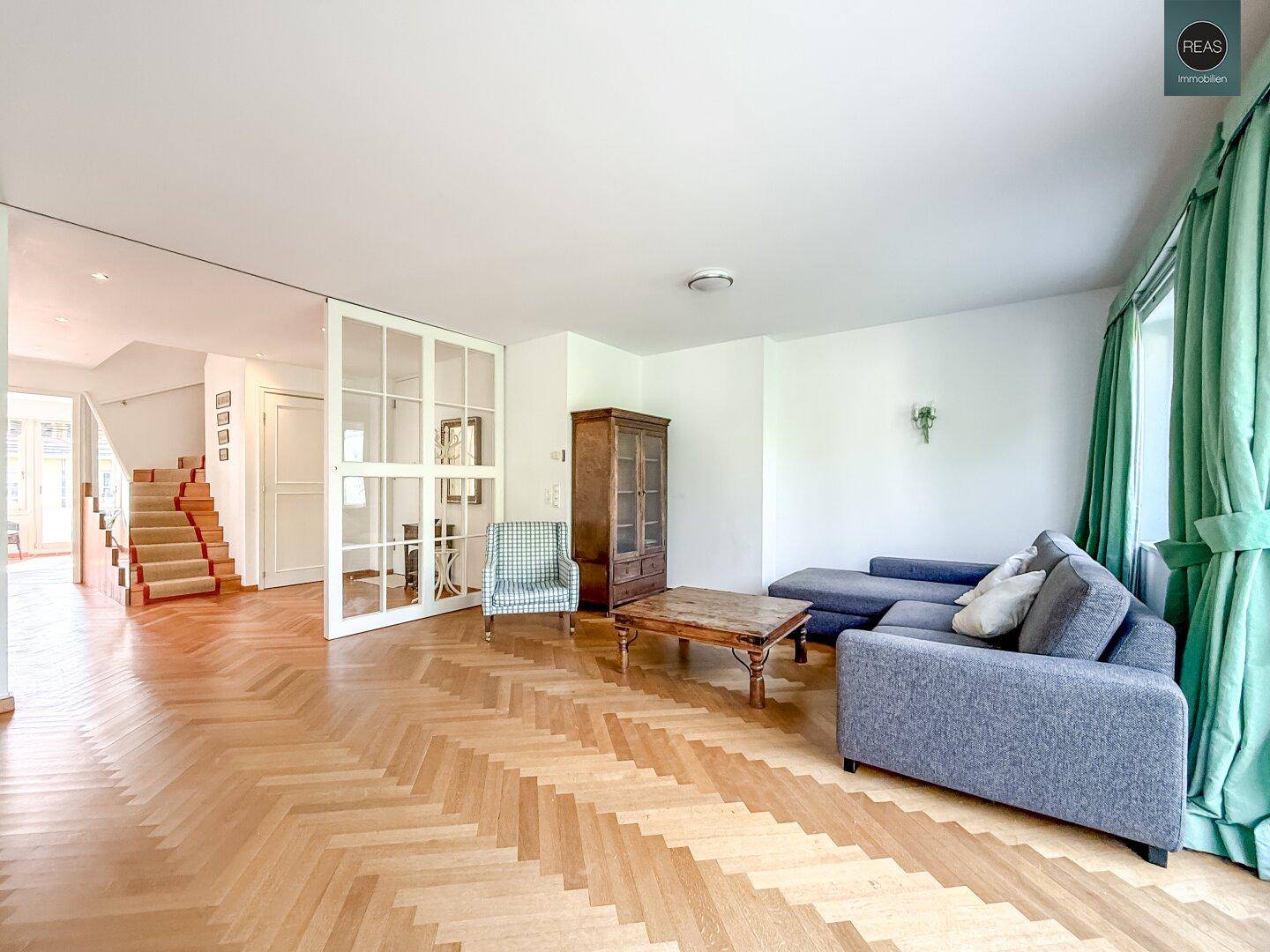 Geräumiges Wohnzimmer mit Parkettboden und einem Durchgang zu einem Treppenhaus.