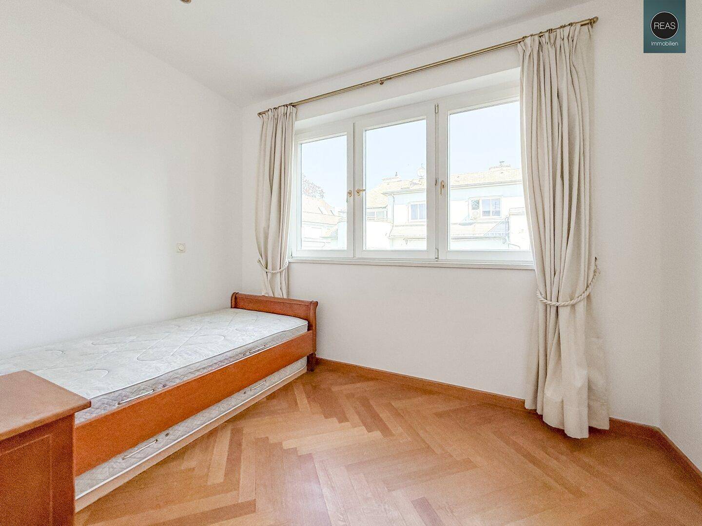 Einfaches Schlafzimmer mit Einzelbett, Parkettboden und einem Fenster mit Stadtblick.