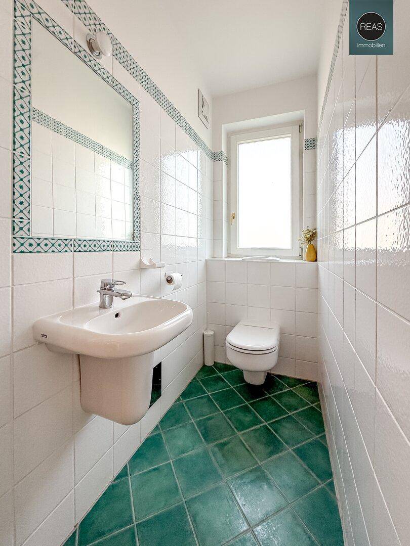 Kleines Badezimmer mit WC, Waschbecken und grünen Bodenfliesen im klassischen Stil.