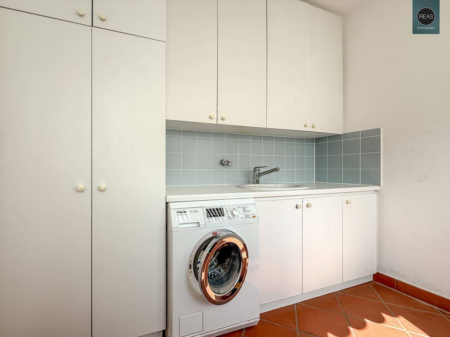 Praktischer Hauswirtschaftsraum mit Waschmaschine, Spülbecken und Stauraum.