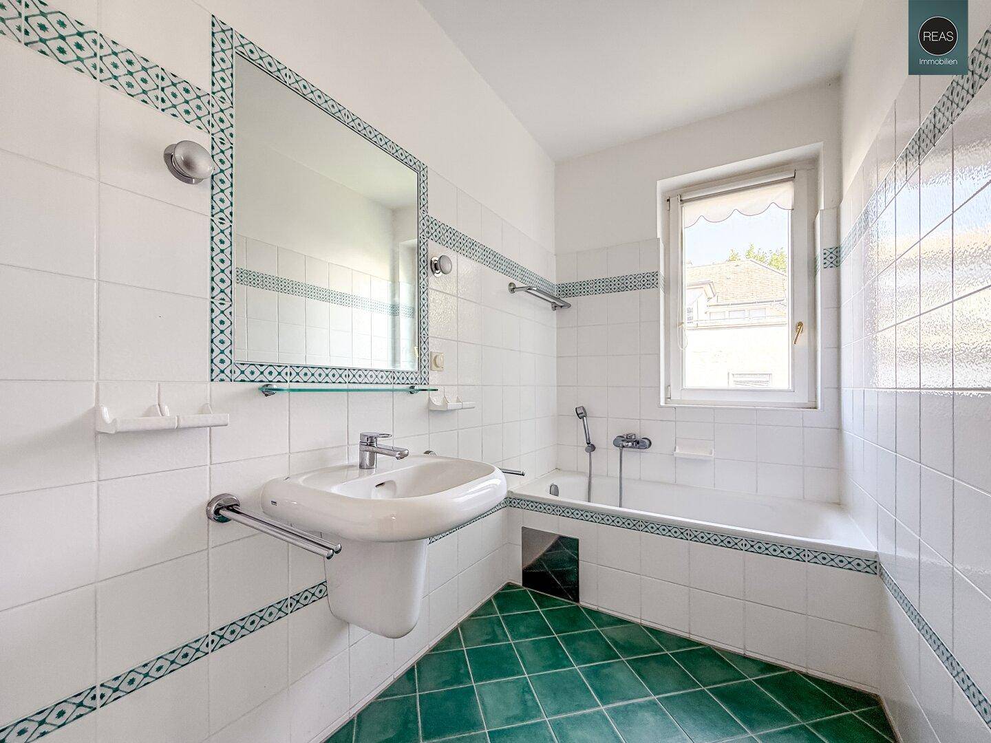 Badezimmer mit Badewanne, Waschbecken und grünen Fliesen im Retro-Stil.