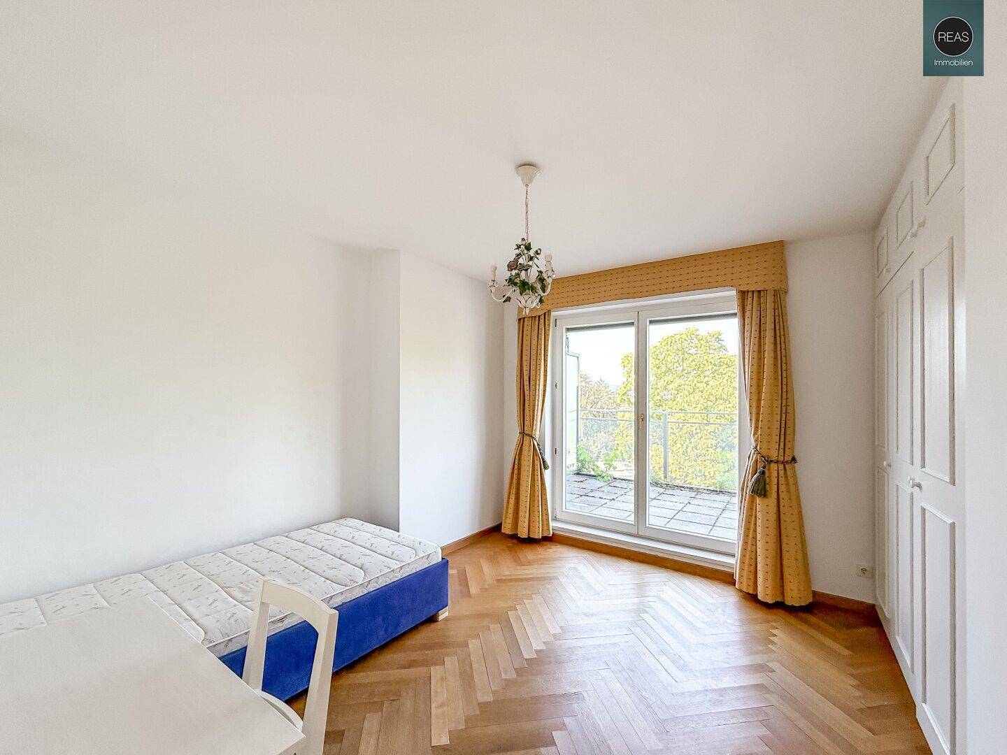 Helles Schlafzimmer mit Einzelbett, Parkettboden und Zugang zu einem Außenbereich.