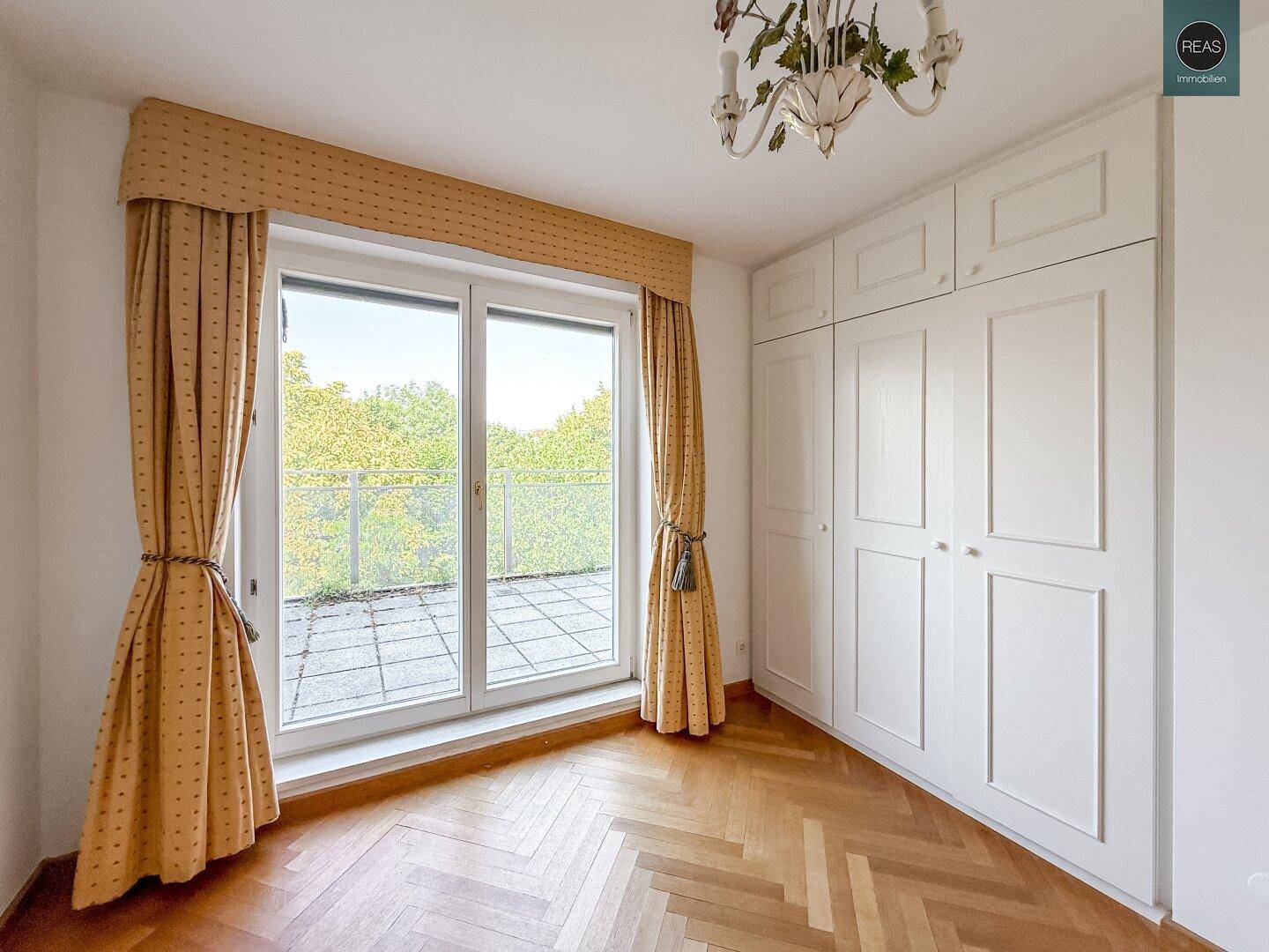 Schlafzimmer mit Einbauschränken, Parkettboden und Zugang zu einem Balkon.