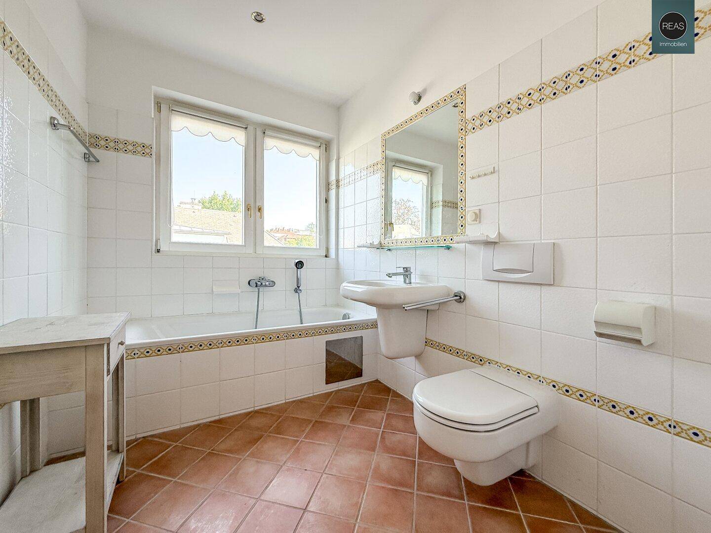 Helles Badezimmer mit Badewanne, WC, Waschbecken und Fenster, ausgestattet mit Fliesenboden und Wandfliesen.