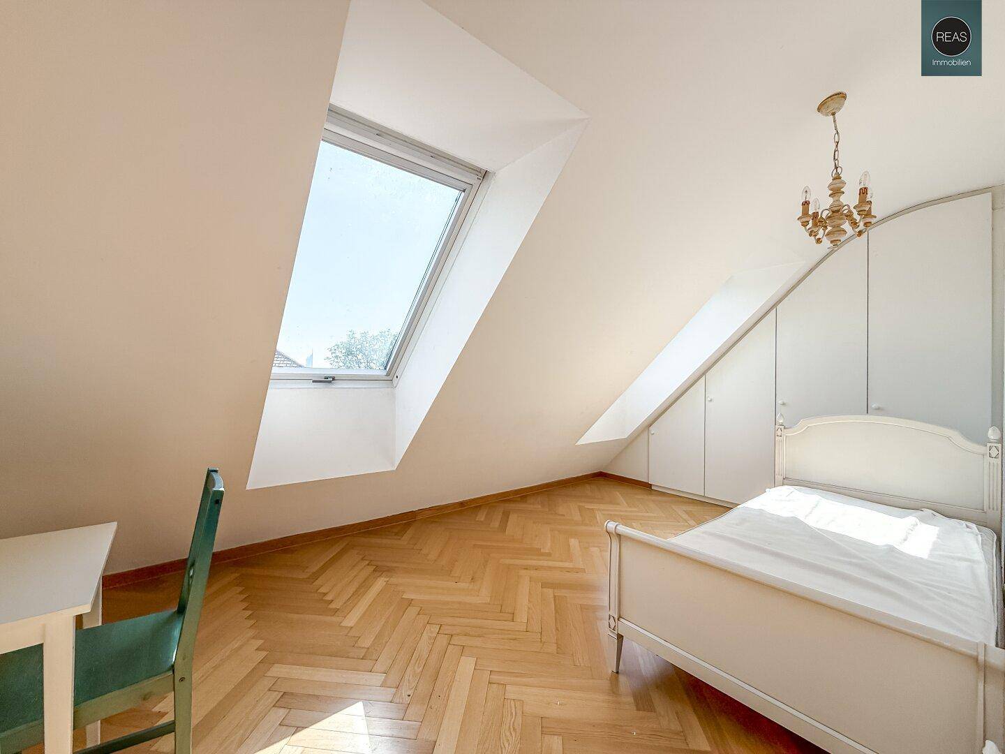 Gemütliches Schlafzimmer im Dachgeschoss mit Dachschräge, Parkettboden und Dachfenster für natürliches Licht.
