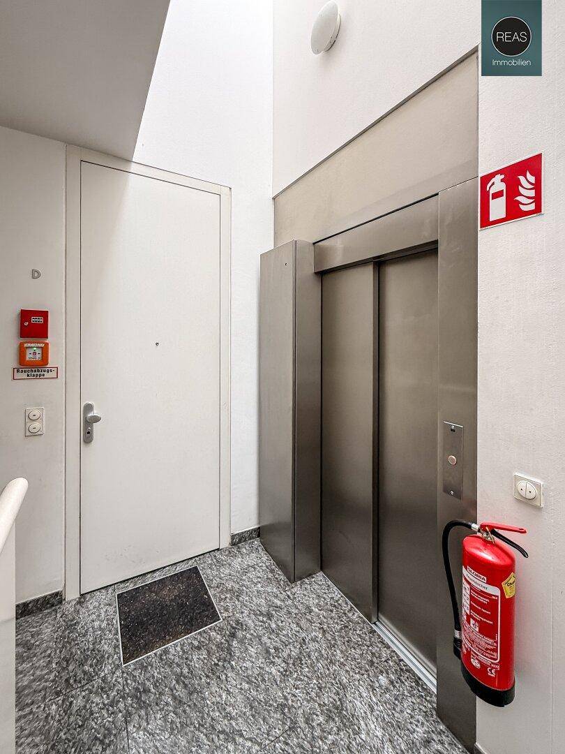Eingangsbereich mit Aufzug, Wohnungstür und Granitboden, ausgestattet mit Feuerlöscher.