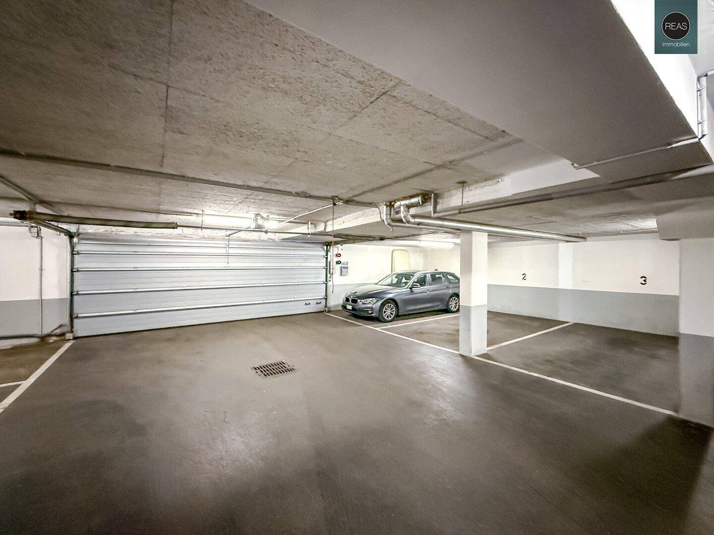 Tiefgarage mit mehreren Stellplätzen und einem Rolltor, gut beleuchtet.