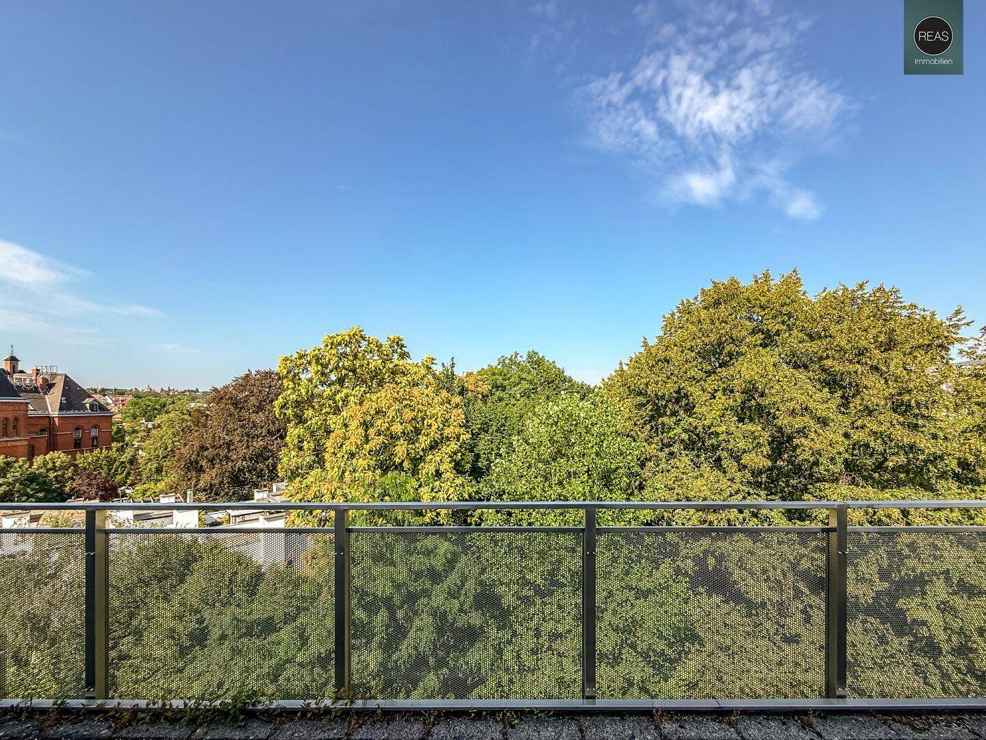 Weitläufiger Blick vom Balkon auf die grünen Baumwipfel und die umliegende Bebauung.