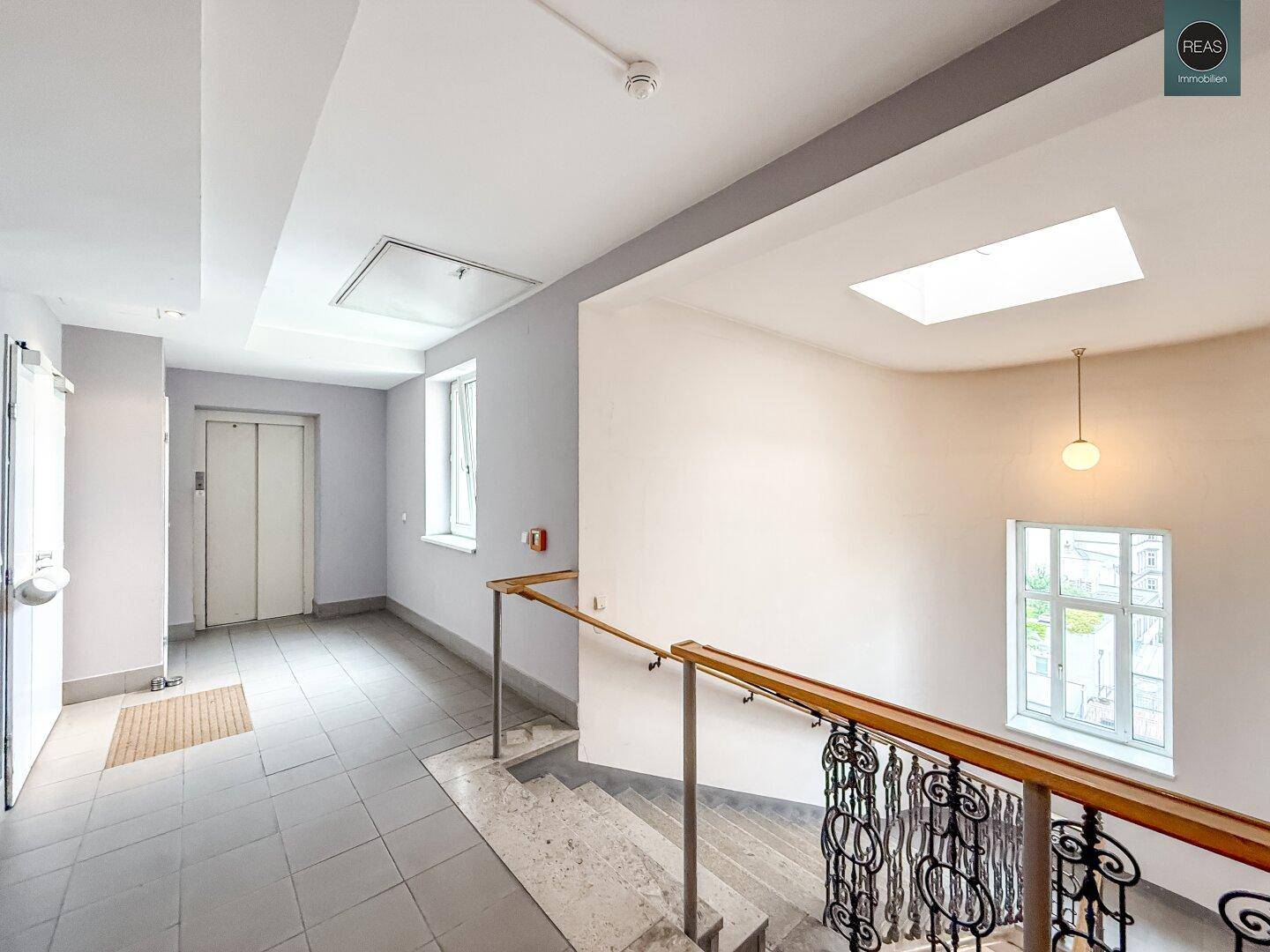 Treppenhaus in einem Altbau mit historischem Geländer und einem Aufzug im Hintergrund.