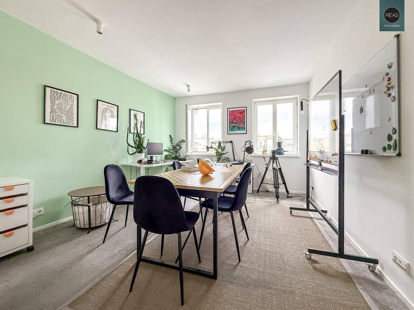 Besprechungsraum mit grüner Akzentwand, großem Holztisch und Whiteboard für Präsentationen.