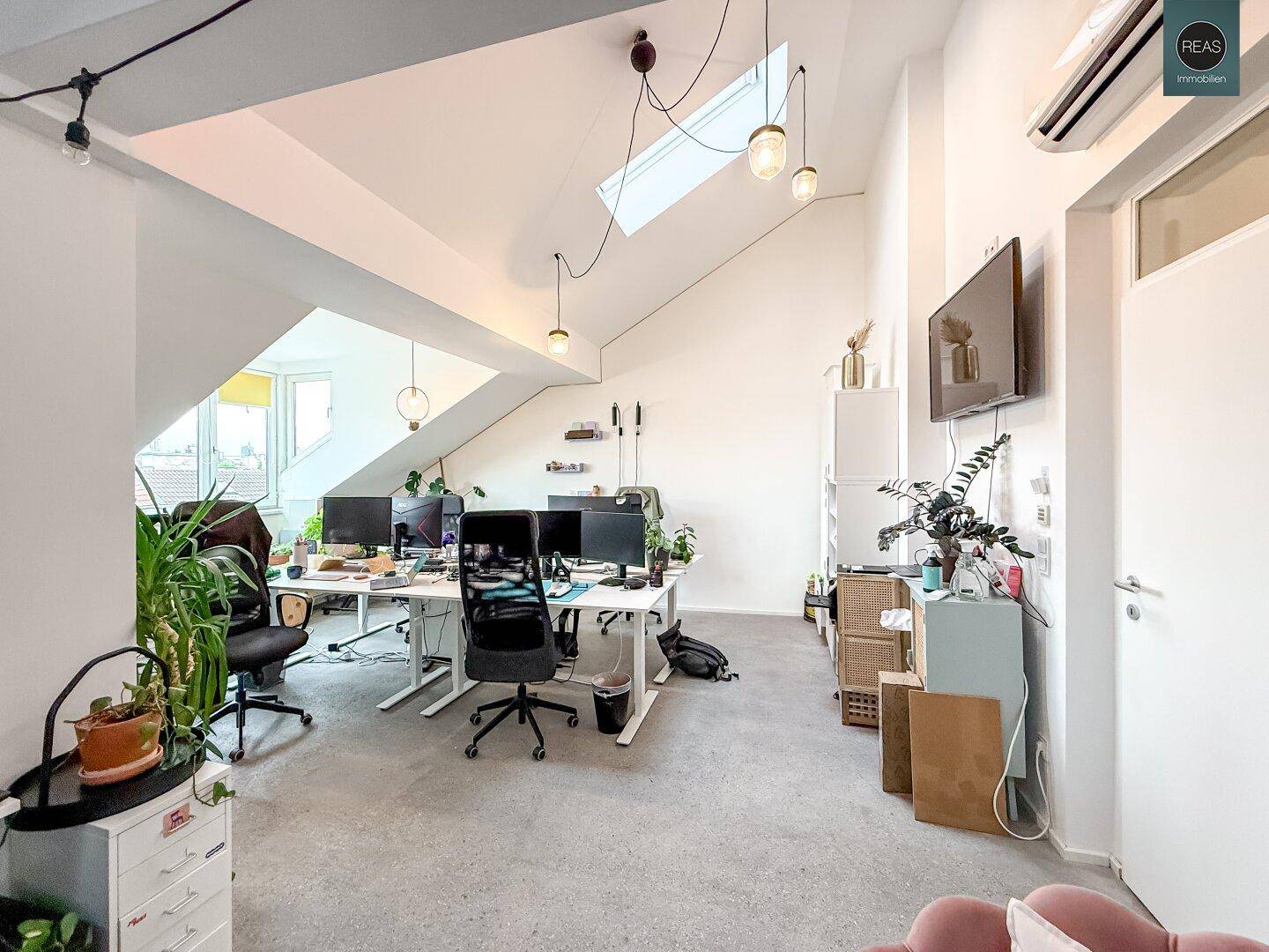 Heller Büroraum mit modernen Arbeitsplätzen, Klimaanlage und einem Fernseher an der Wand.