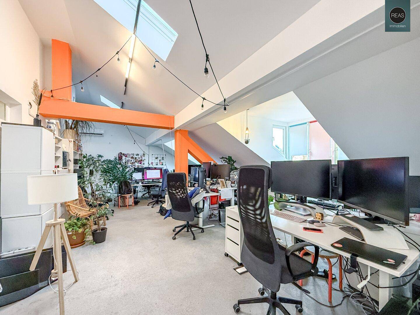 Modernes Büro mit offener Gestaltung, vielen Pflanzen und auffälligen orangefarbenen Trägern.