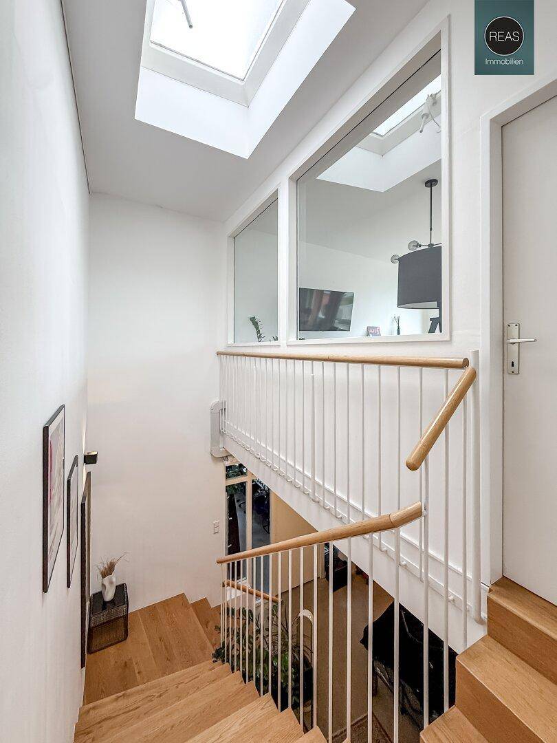 Helle Holztreppe mit Oberlicht und Fenster, das den Blick in einen angrenzenden Raum freigibt.