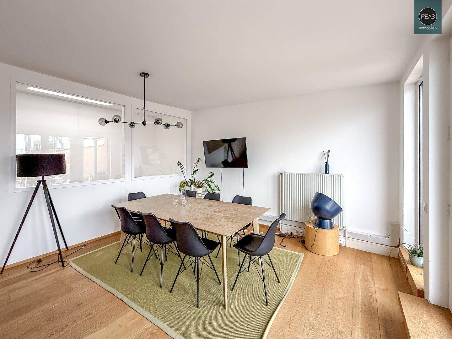 Esszimmer mit Holzboden, großem Fenster und modernem Esstisch mit schwarzen Stühlen.